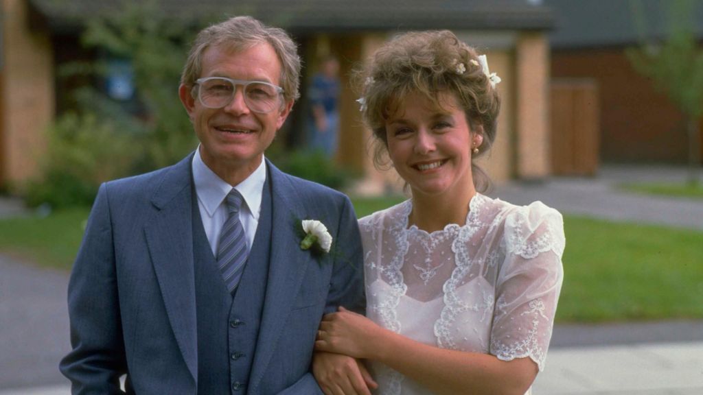 Rothwell and Burton dressed in wedding attire in character during the filming of Brookside. He wears a suit while she wears a laced wedding dress style shawl.