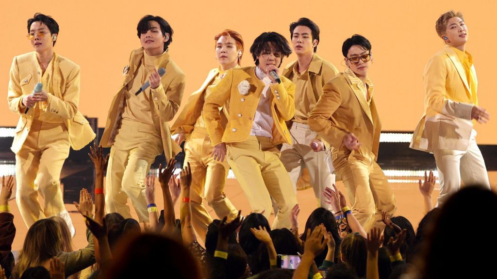 BTS performing on stage in matching yellow suits. 