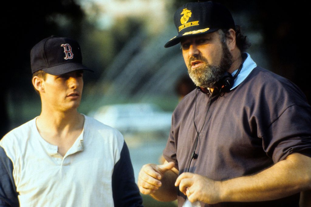 Tom Cruise in a baseball shirt and cap looking at Rob Reiner, speaking on the set of A Few Good Men with heaphones and cap