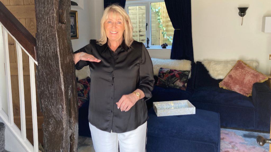 A woman with long blonde hair stands in a room holding her hand at chest height to indicate how high the water reached