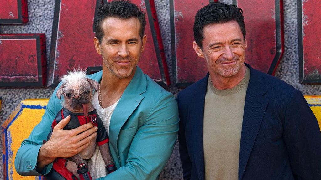 Peggy dog being held by Ryan Reynolds who is standing next to Hugh Jackman