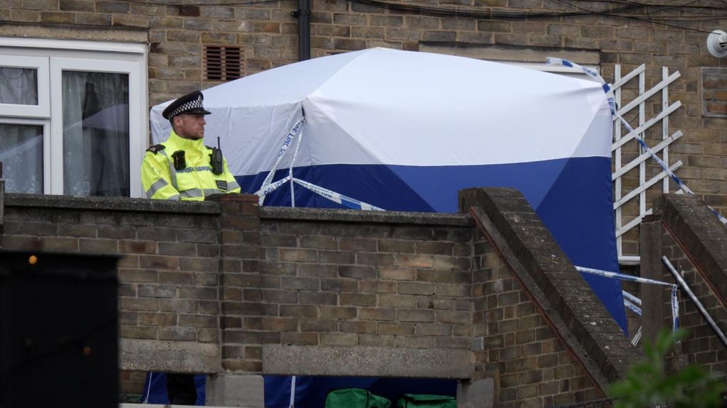 A blue and white police tent and a police officer standing outside a house