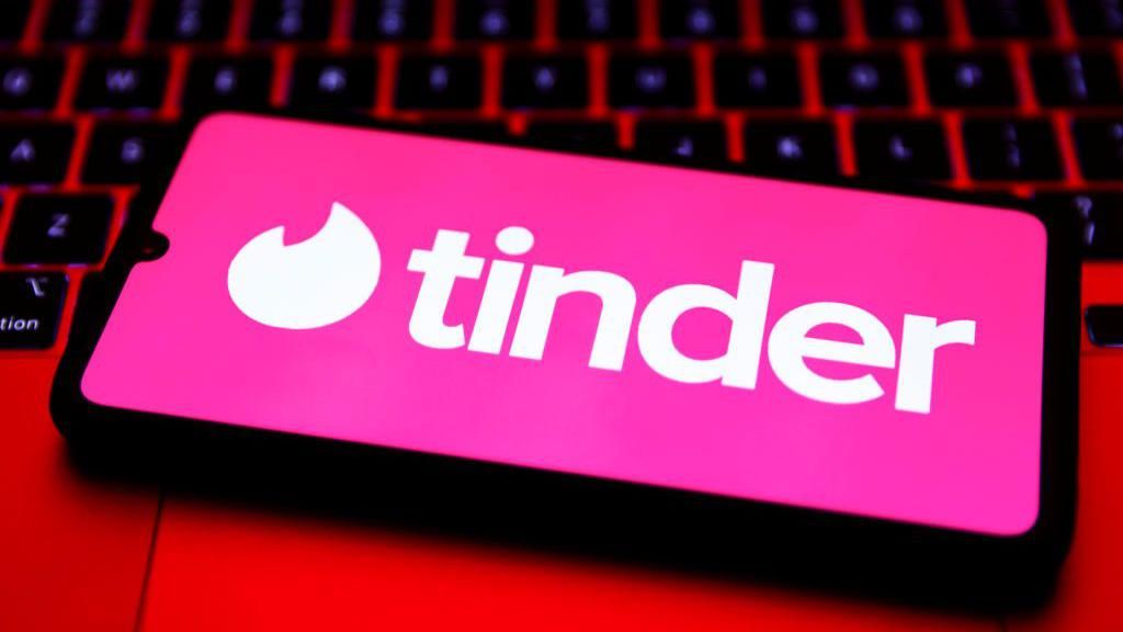 Tinder logo displayed on a smartphone on a computer keyboard bathed in red light 