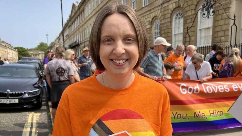 A woman in an orange top smiling at the camera.