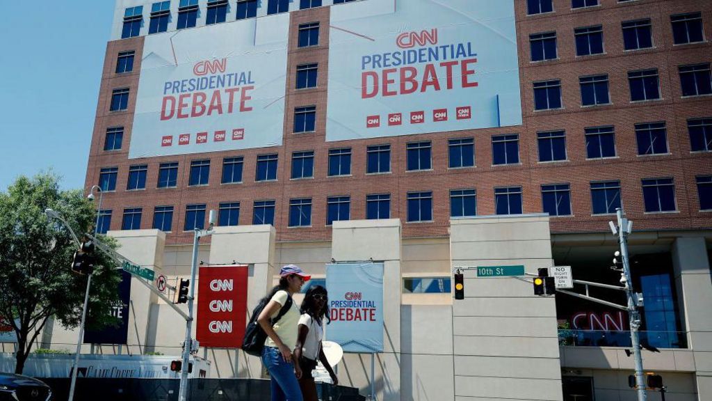 People walk past signs advertising the CNN presidential debate outside of their studios on June 25, 2024 in Atlanta, Georgia.