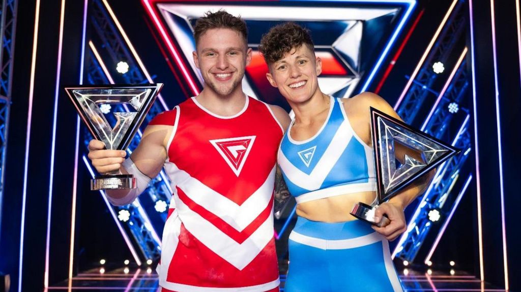 A man in red and a woman in blue holding their trophies.
