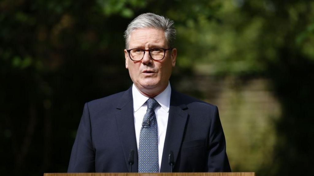 Prime Minister Sir Keir Starmer wearing glasses and a suit delivering a speech in the open air