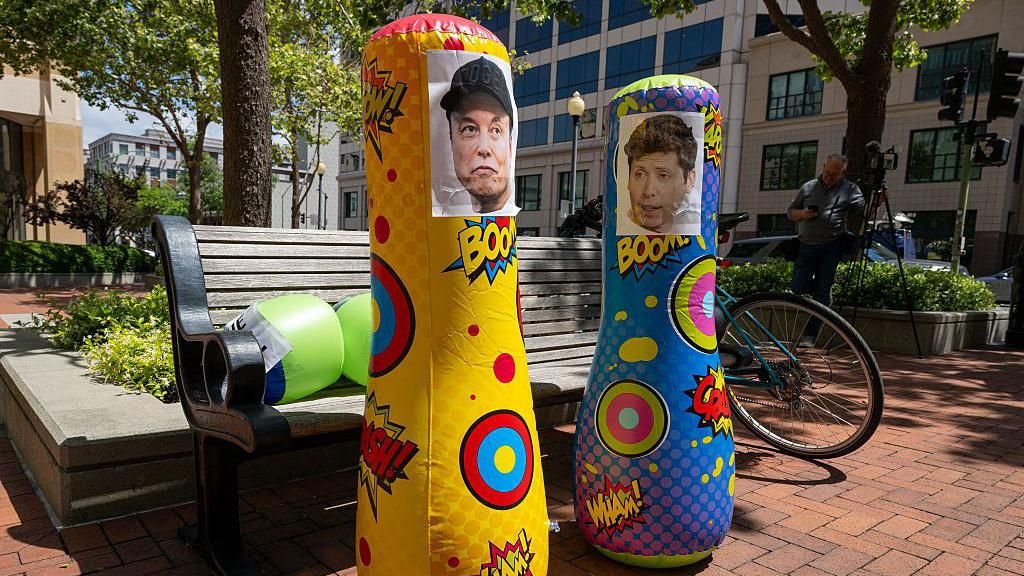Punching bags with the faces of Musk and Altman seen outside of court