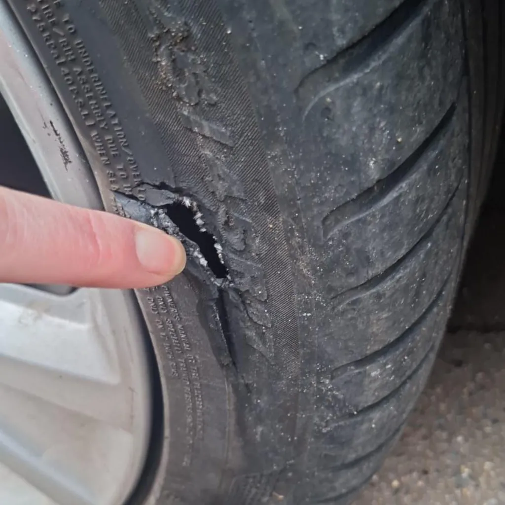 A finger pointing to a deflated tyre with damage to the tyre wall