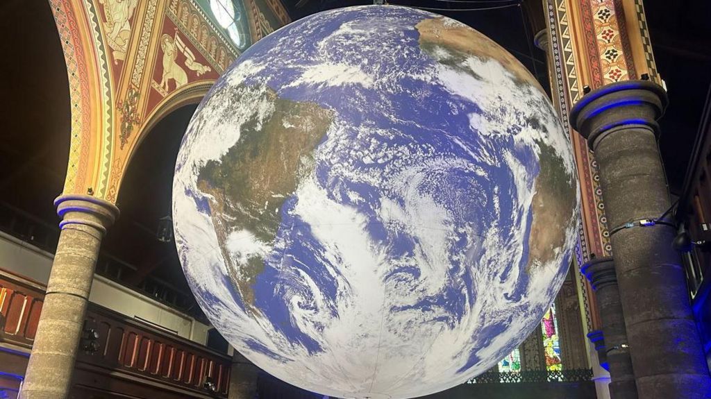 Globe features Nasa imagery printed on fabric hanging from a church ceiling