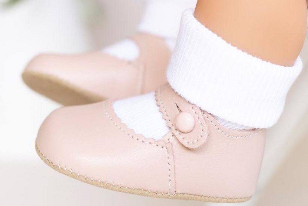 A pair of pale pink baby shoes with stitching.