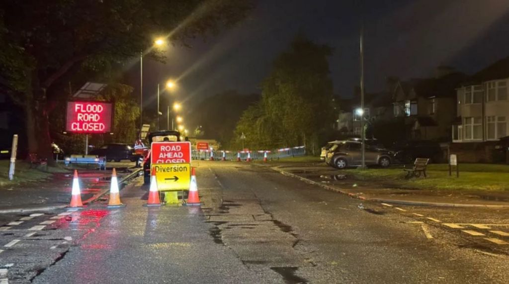 Queens Drive in Liverpool at night, with cones, temporary fencing and three separate signs reading: Flood Road Closed, Road Ahead Closed and Diversion.  