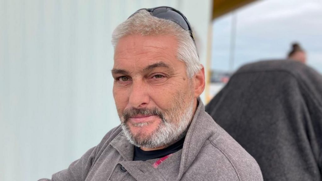 Christopher looking at the camera. He has a beard and is wearing a grey jumper.