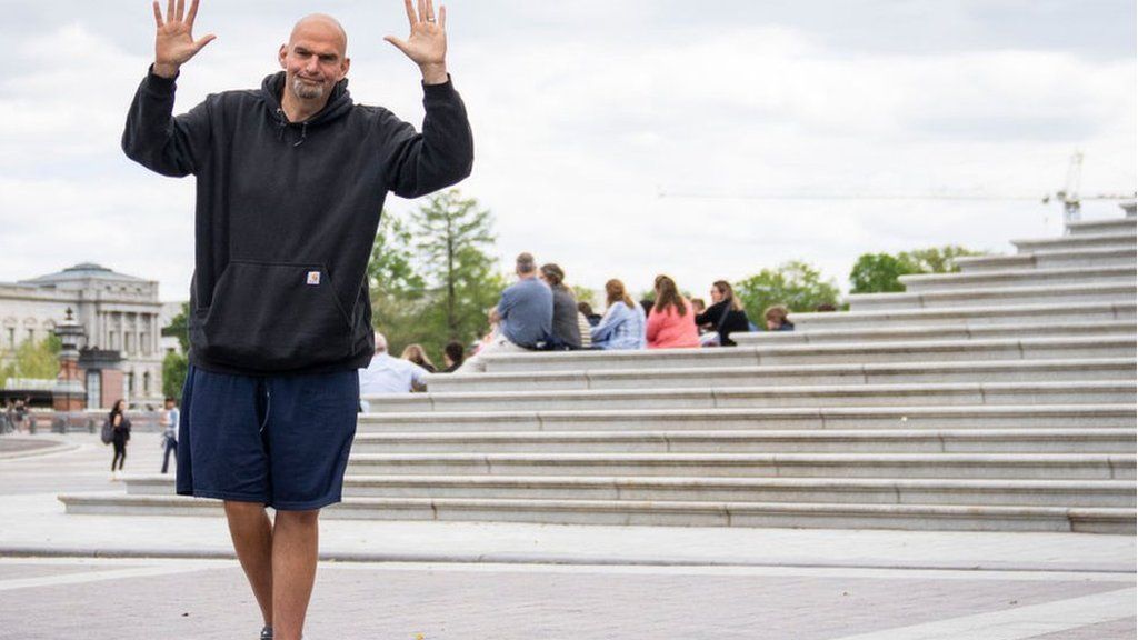 John Fetterman in black sweatshirt and blue gym shorts in front of steps to the Capitol