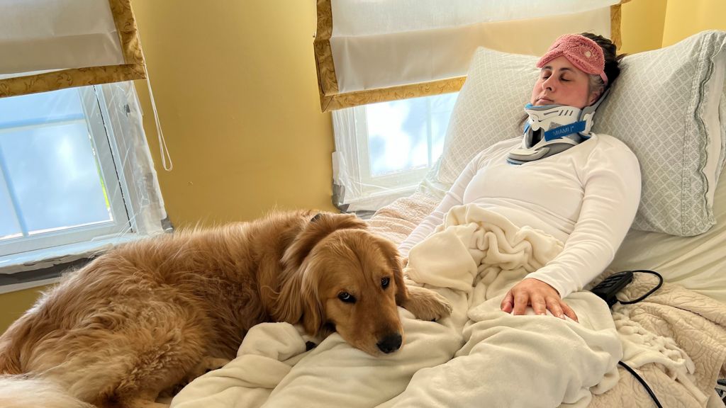 Georgia McGinty in a hospital bed in a neck brace, with her dog lying next to her