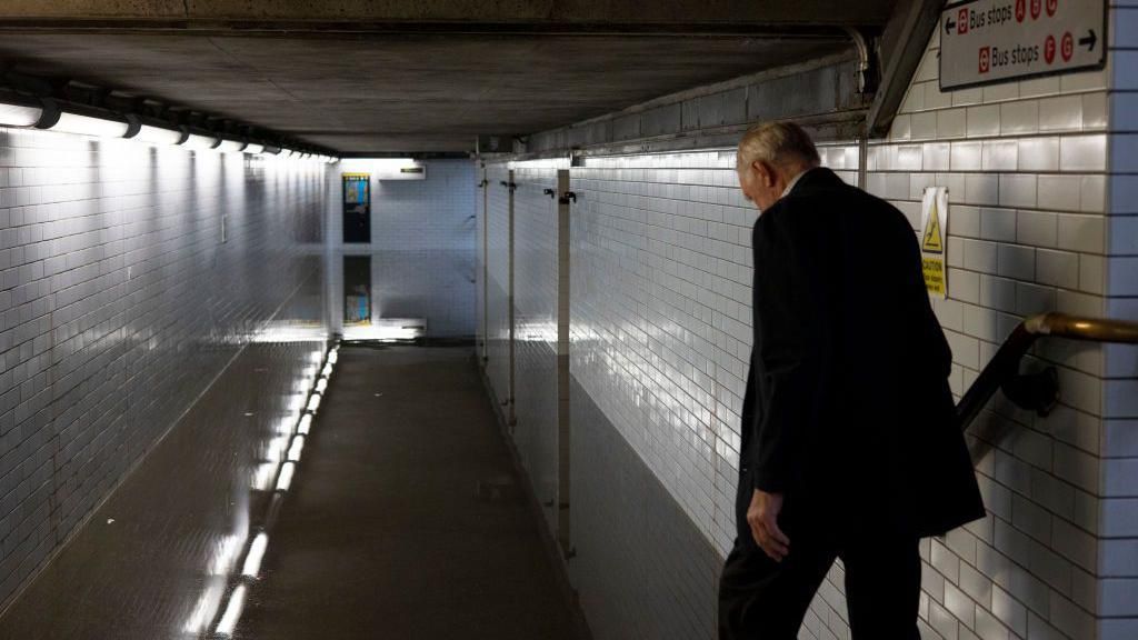 A man trying to walk across a flooded Westminster tube station underground pass.