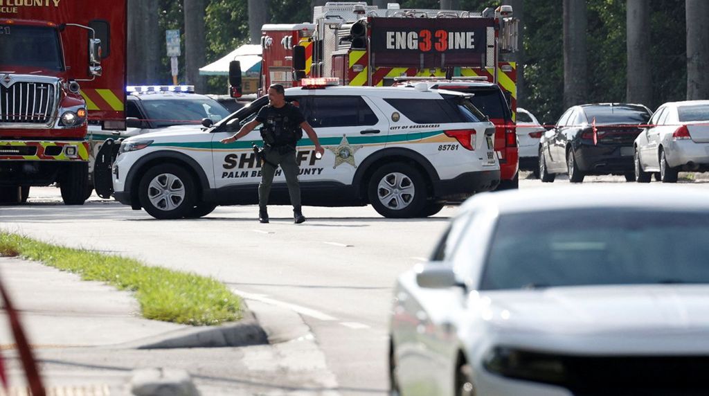 A police officer gestures in front of a sheriff's vehicle and a fire engine, with other cars to the right of frame, in West Palm Beach, Florida, U.S. September 15