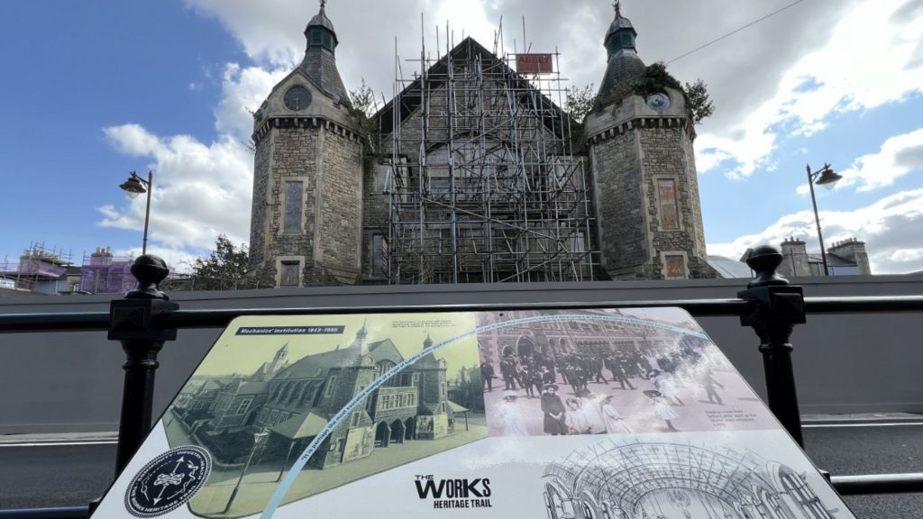 An information board showing the Mechanics' Institute in its heyday, overlooking the current building which has scaffolding on it