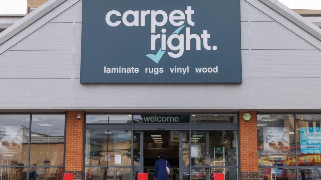 Exterior view of a Carpetright store with a woman walking into the shop under a sign saying Welcome