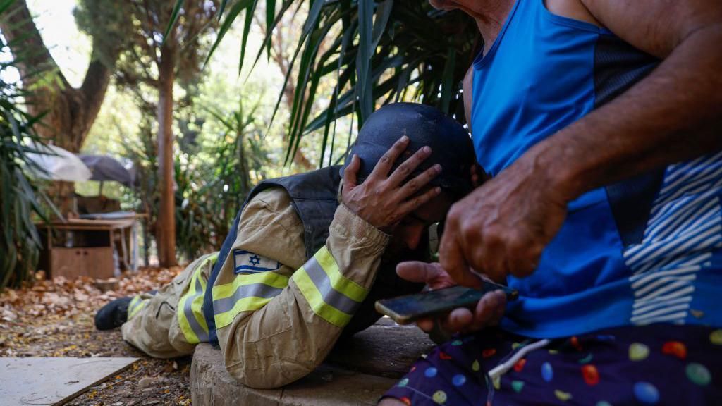 An Israeli firefighter and a resident take cover as sirens sound to warn of rockets launched from southern Lebanon, in Kiryat Shmona in northern Israel near the Lebanese border on June 19, 2024.