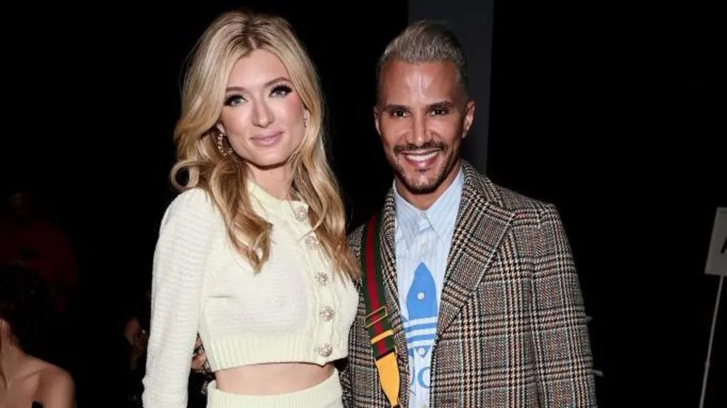 Sophie Sumner poses alongside former America's Next Top Model judge Jay Manuel. Sophie wears a yellow knit cardigan and has blonde hair and Jay wears a tweed jacket over a blue shirt. He has short cropped hair. 