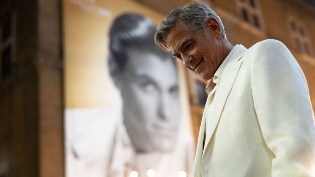 George Clooney in Jay Kelly, wearing a white suit and smiling at the gound