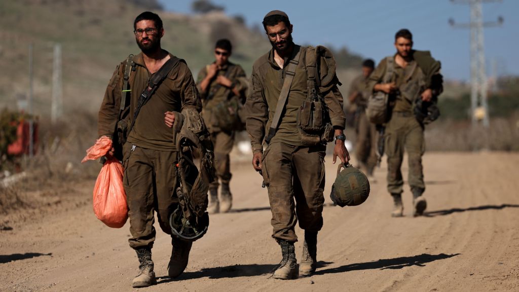 Five Israeli soldiers, dressed in dark green army uniform and combat boots walk along a dusty road with their belongings as they return to Israel from Lebanon