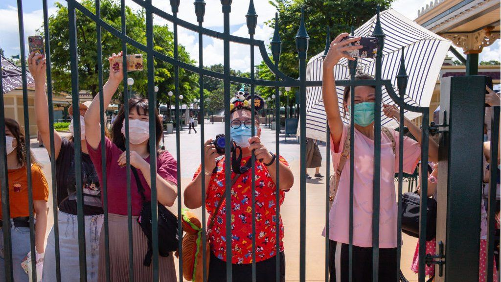 Hong Kong Disneyland visitors wearing protective face masks take photographs behind a fence.