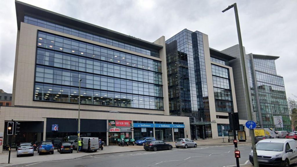 A Google maps image of a large, glass-fronted, six-storey office block in central Redhill with restaurants and shops on the bottom floor and cars visible on the road below 