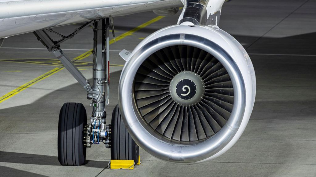 A closeup of a jet engine on an Airbus A320 which is parked at an airport at night.