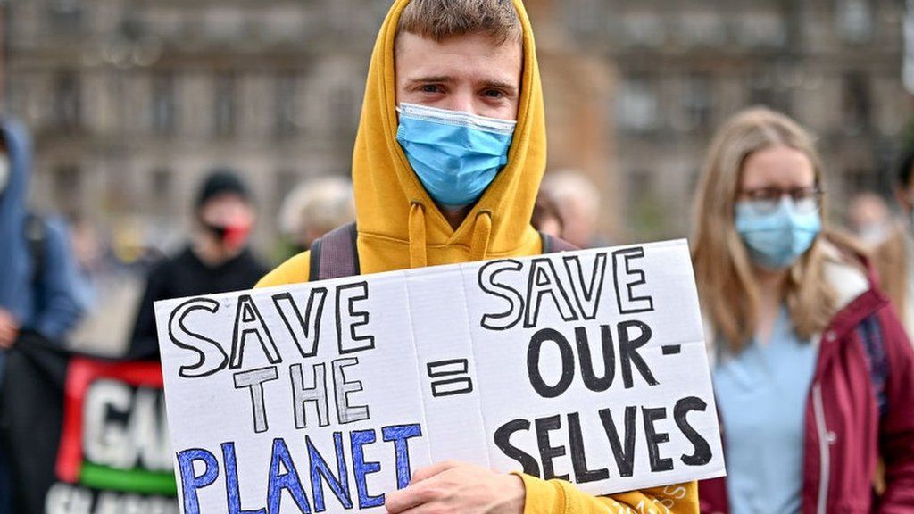 A protestor holds a placard saying 'Save Our Planet = Save Our Selves'