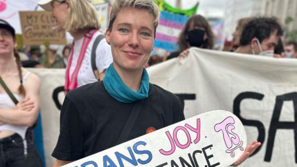 An attendee of the event holding a sign, of which you can just see the words "trans" written in blue and "joy" written in pink against a white background