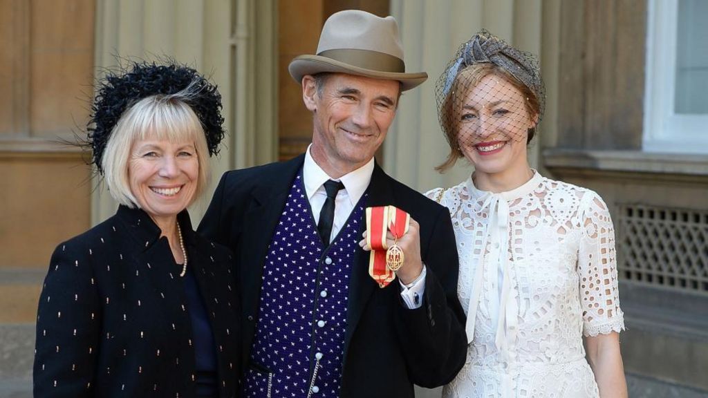 Claire wears a black headband and a black embroided jacket with a string of pearls as she stands next to her husband Sir Mark outside Buckingham Palace after he was knighted 