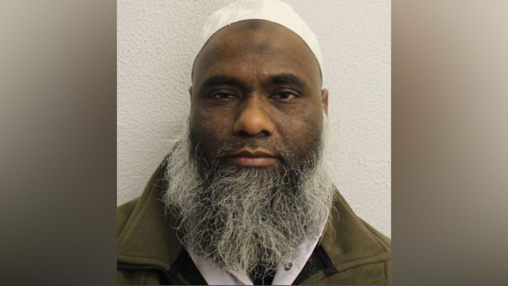 A man with a long grey beard looks at the camera