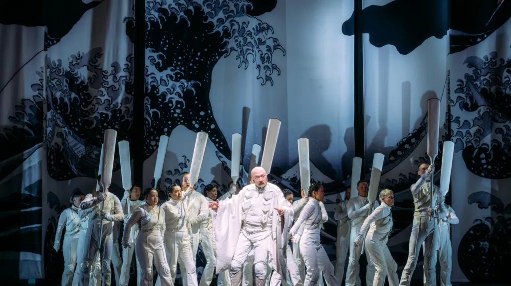 Performers on stage dressed in white with Hokusai's The Great Wave painting in the background.