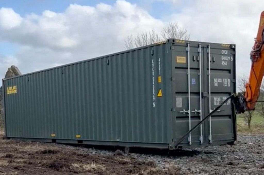 A green shipping container on muddy ground