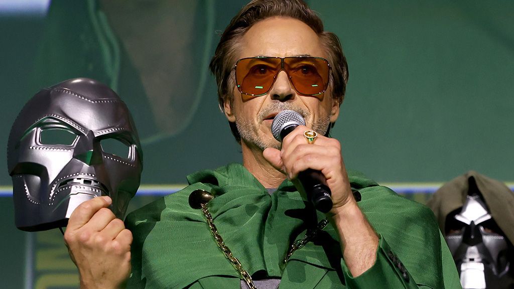 Robert Downey Jr holds Dr Doom mask in his right hand while wearing a green cloak on stage at Comic Con