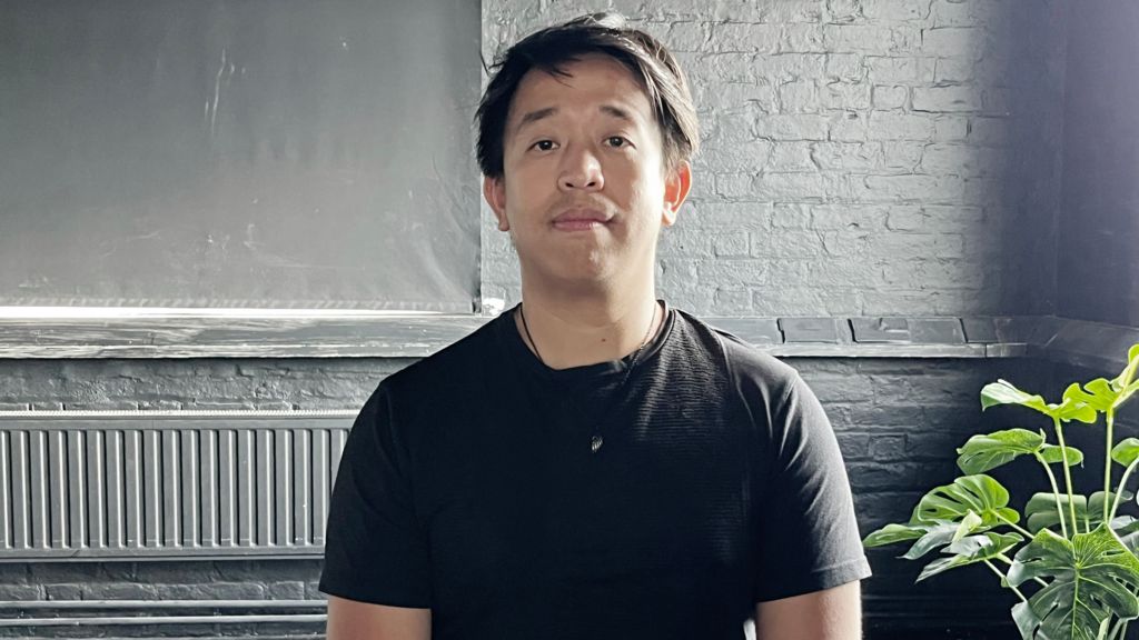 Andrew Kaung, sitting facing the camera in a loft-style room, wearing a black T-shirt