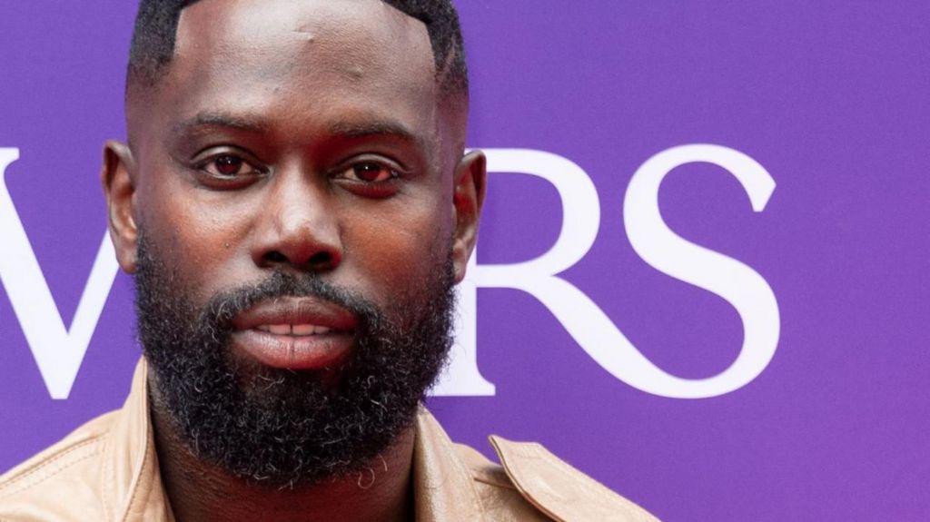 Ghetts at the Ivor Novello Awards 2025. Image shows close-up of the rapper with a purple and white banner in the background. He has short-shaven black hair and a full short beard