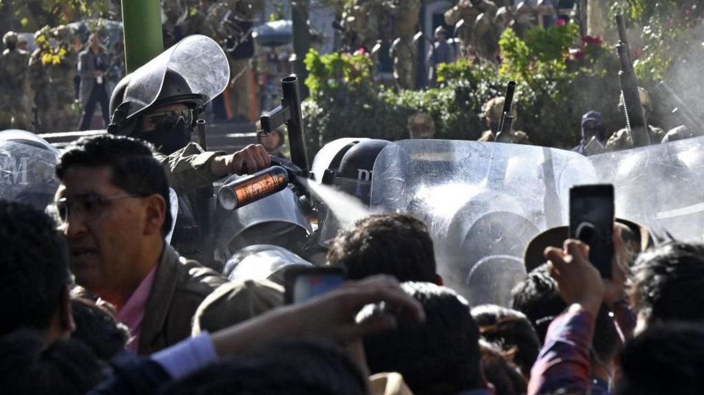 A soldier sprays people with tear gas