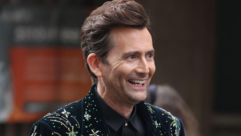 David Tennant smiling in a black suit with a bejewelled collar 