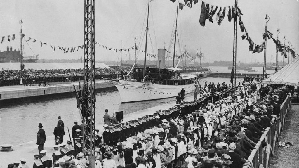 A black and white photograph of a ship arriving at London's Royal Docks and the docks full of people waiting for its arrival