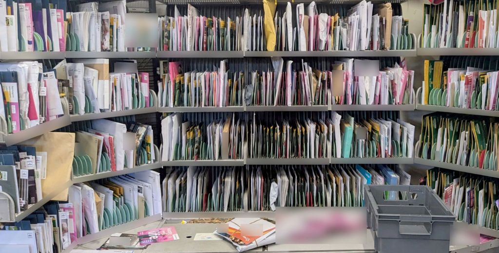Lots of envelopes in different sizes and colours sit in a sorting cabinet at a Royal mail depot.