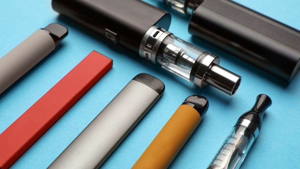 Different electronic cigarettes on light blue background, closeup
