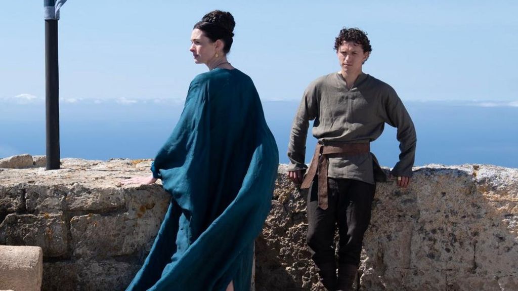 Anne Hathaway as Penelope and Tom Holland as Telemachus, together atop a castle overlooking the sea