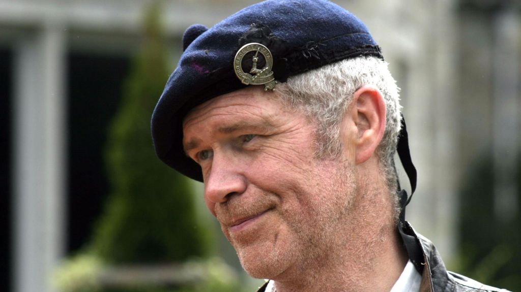 Sandy Morton, smiling in close-up in a tartan hat. He has grey hair.