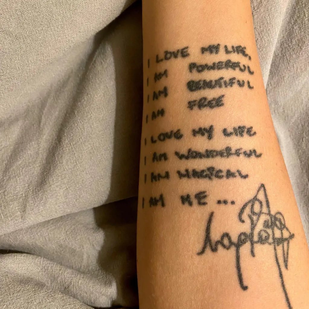 A close-up of an arm with lyrics by Robbie Williams tattooed on it, as well as Williams's signature.