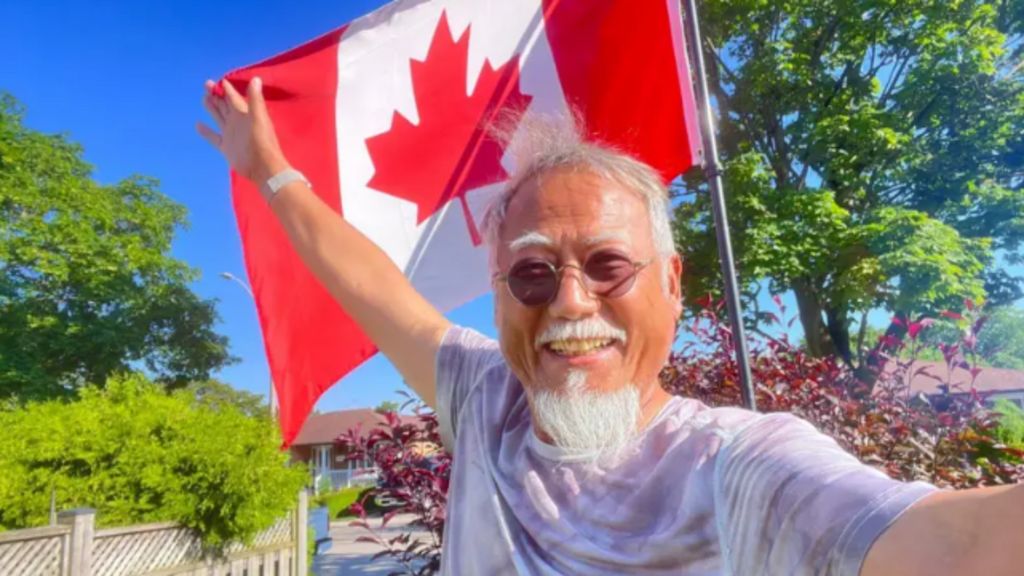 Dong Guangping posing in front of a Canadian flat, with his right hand holding the flag