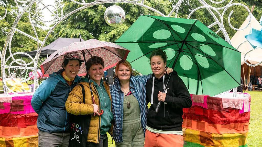 Four women stand under umbrellas