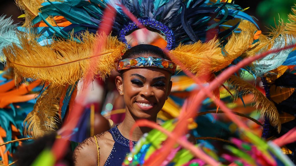 A woman in colourful feathers and a navy blue sequinned top smiles at the camera.